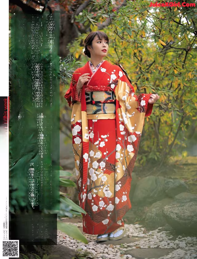 A woman in a red kimono standing in front of a tree.