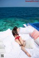 A woman in a red bikini laying on a bed by the ocean.