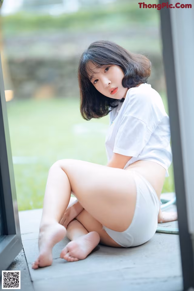 A woman in a white shirt and white panties sitting on the ground.