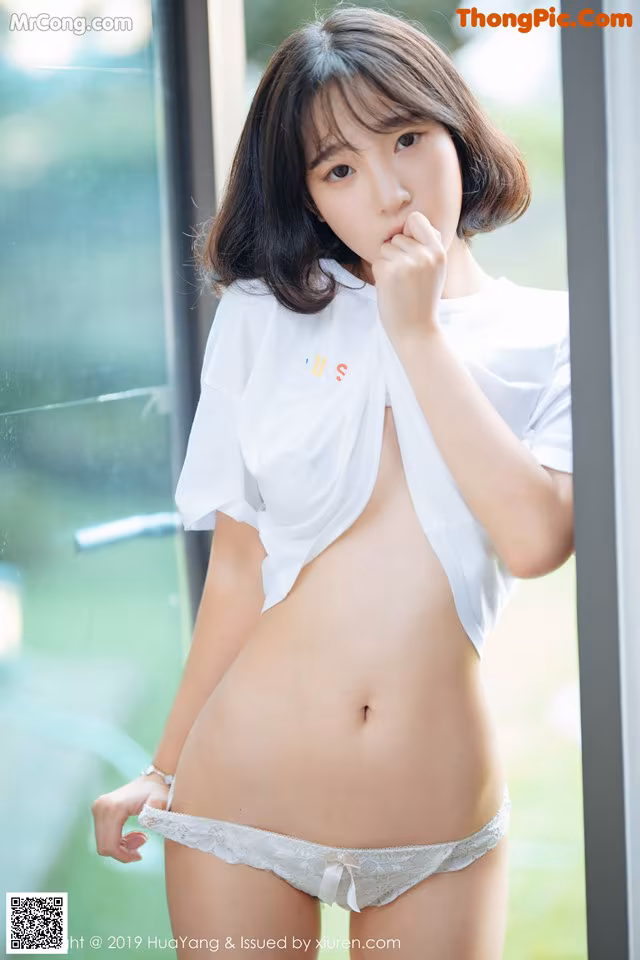 A woman in a white shirt and panties posing for a picture.