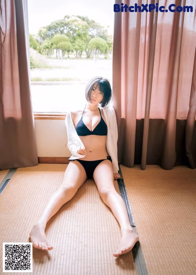 A woman in a black bikini sitting on a tatami mat.