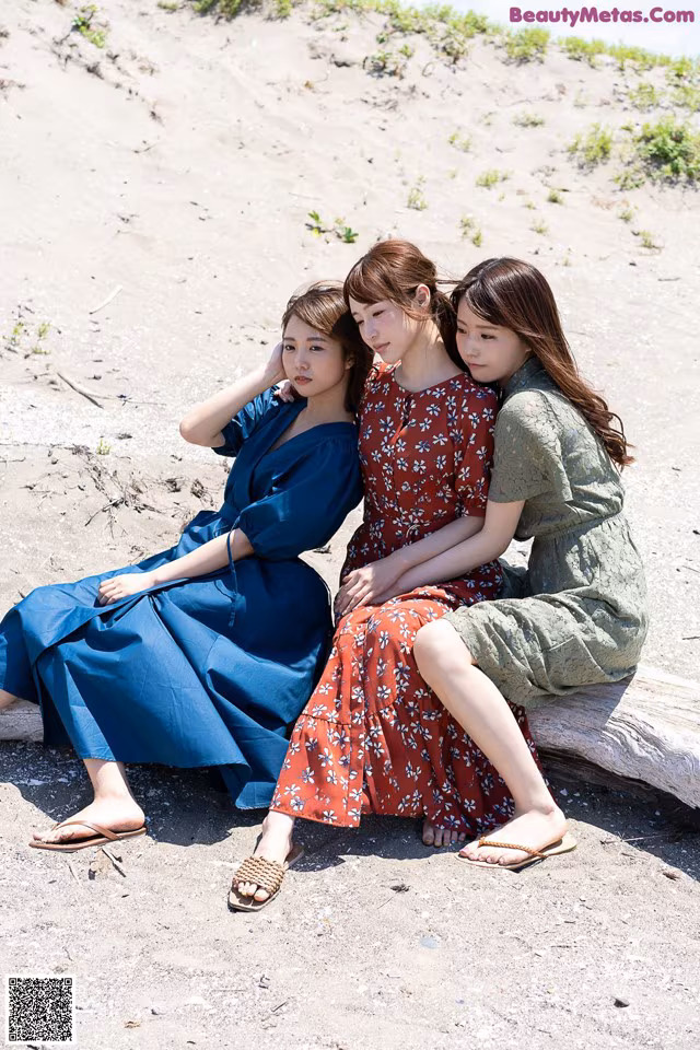A group of three women sitting on top of a log.