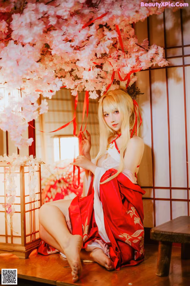 A woman in a red and white kimono sitting under a cherry blossom tree.