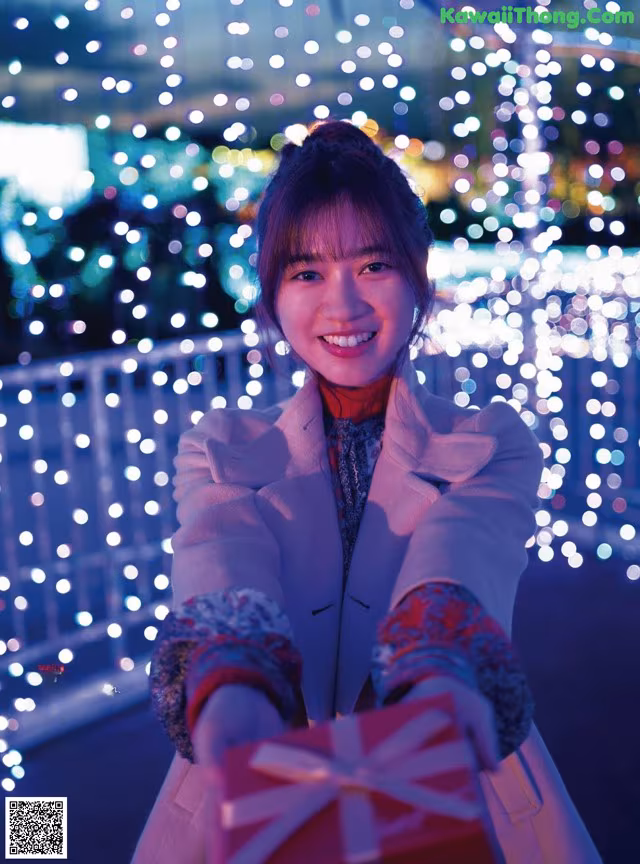 A woman holding a red gift box in front of a ferris wheel.