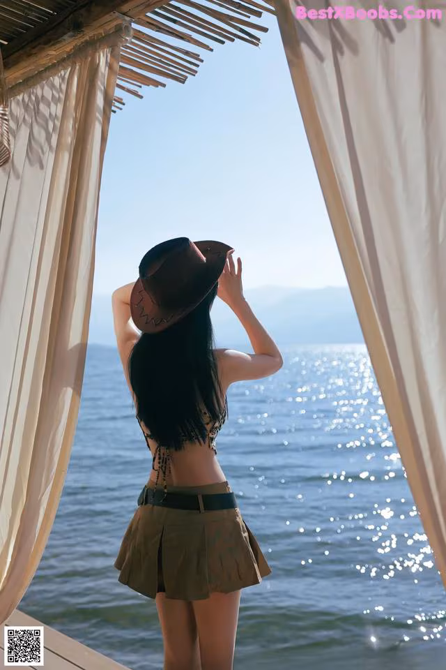 A woman in a hat is standing by the water.