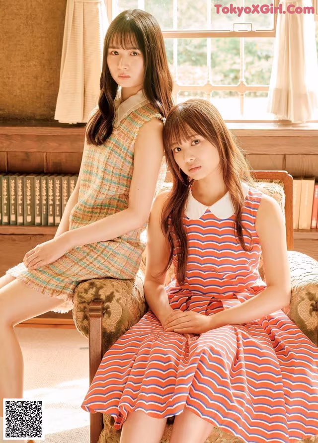 Two young women sitting on a chair in front of a window.