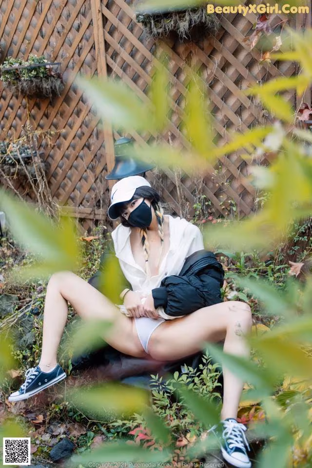 A woman wearing a face mask sitting on a bench in the woods.