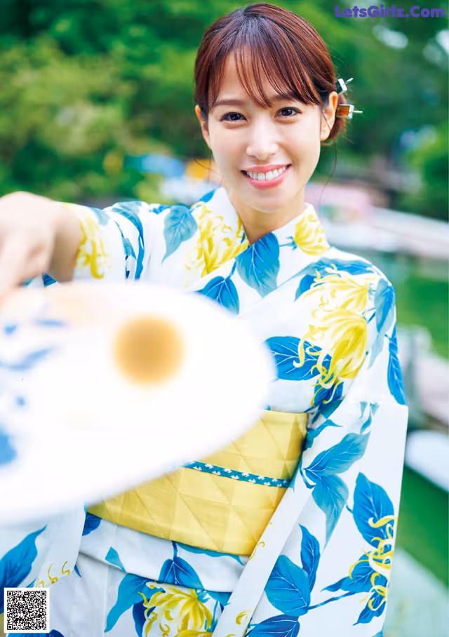 A woman in a blue and yellow kimono holding a fan.
