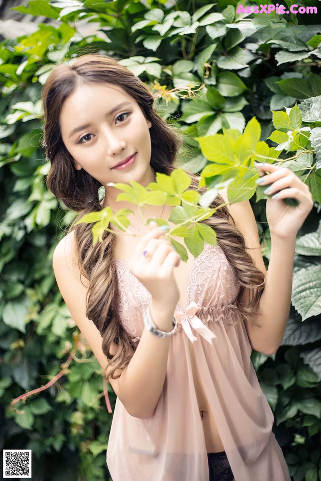 A woman in a pink lingerie posing in front of a bush.