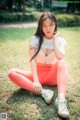 A woman sitting on the grass in a white shirt and orange leggings.