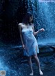 A woman in a white dress standing in front of a waterfall.