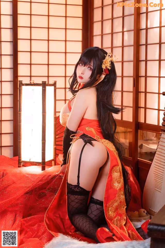 A woman in a red and black lingerie sitting on a bed.