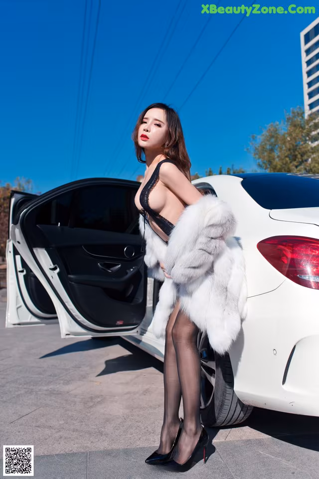 A woman in a white fur coat standing next to a white car.