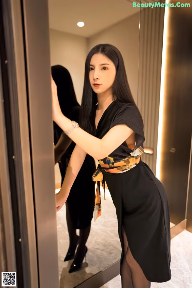 A woman in a black dress standing in front of a mirror.