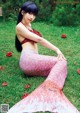 A woman in a mermaid tail sitting on the grass.