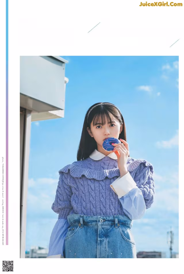 A woman in a blue sweater and denim skirt holding a lollipop.