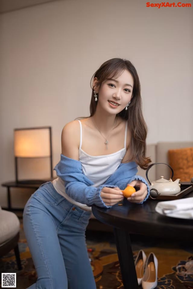 A woman sitting at a table holding an orange.