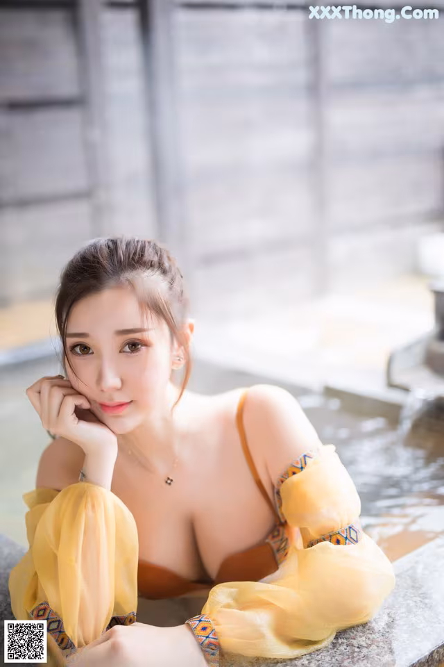 A woman in a yellow dress sitting in a bathtub.