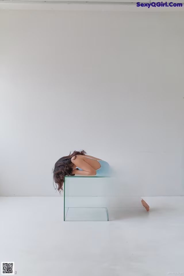 A woman in a blue bathing suit sitting on a clear box.