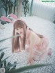 A woman in a pink bunny costume crouching on a bed of white pebbles.