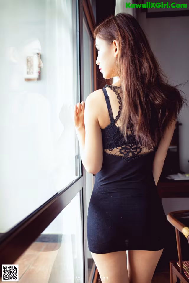 A woman in a black dress looking out a window.